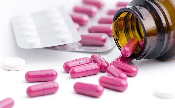 Bright pink capsules and white pills in a blister pack and spilling out of a brown bottle onto a white surface